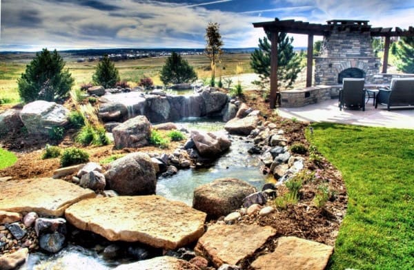Backyard pond with a natural rock waterfall, stream, and a patio with pergola and fireplace.