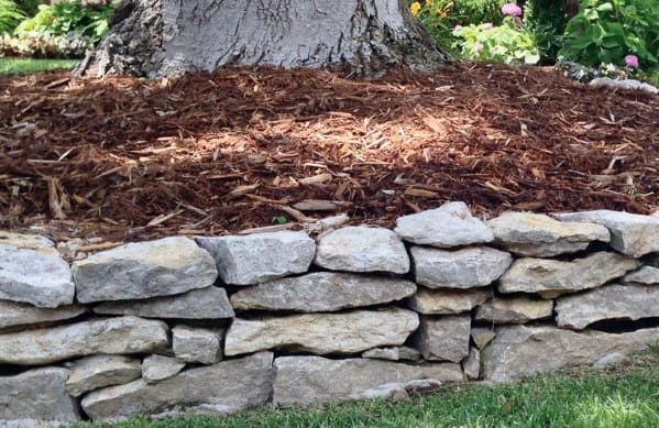 A natural stone border around the base of a tree, with mulch filling the inner circle, creating a neat and rustic garden feature