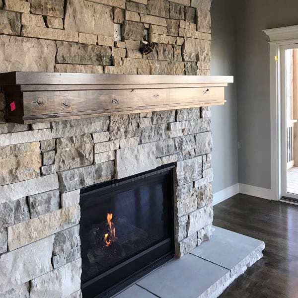 Natural stone fireplace with rustic wooden mantel and modern gas insert.