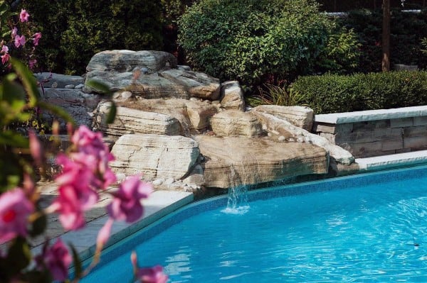 Backyard pool with natural stone waterfall and lush greenery in the background.