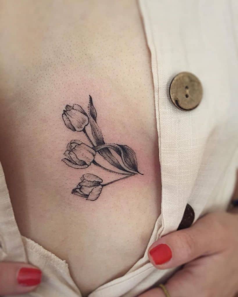 A delicate black and grey tulip tattoo on the ribcage, featuring three blooming flowers with fine shading and soft, flowing leaves.