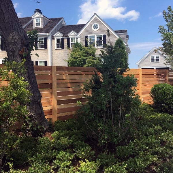 Horizontal wooden fence surrounding a lush garden in front of a classic house.