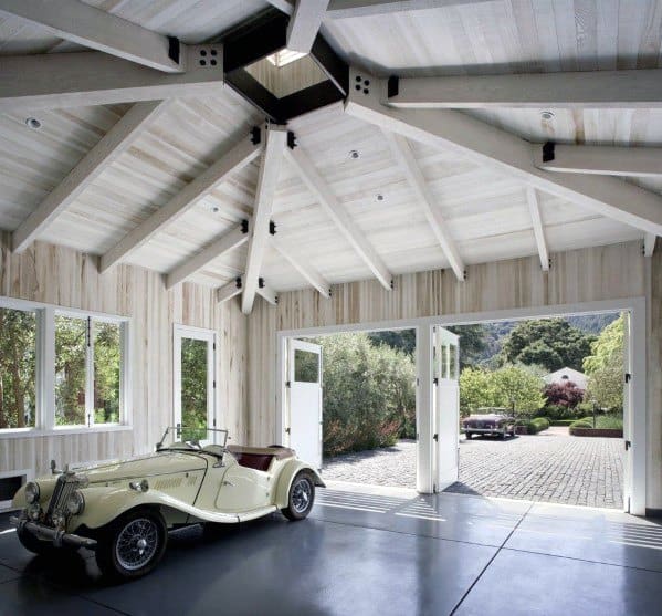 Bright garage with vaulted whitewashed beams, open barn doors, and a vintage convertible car.