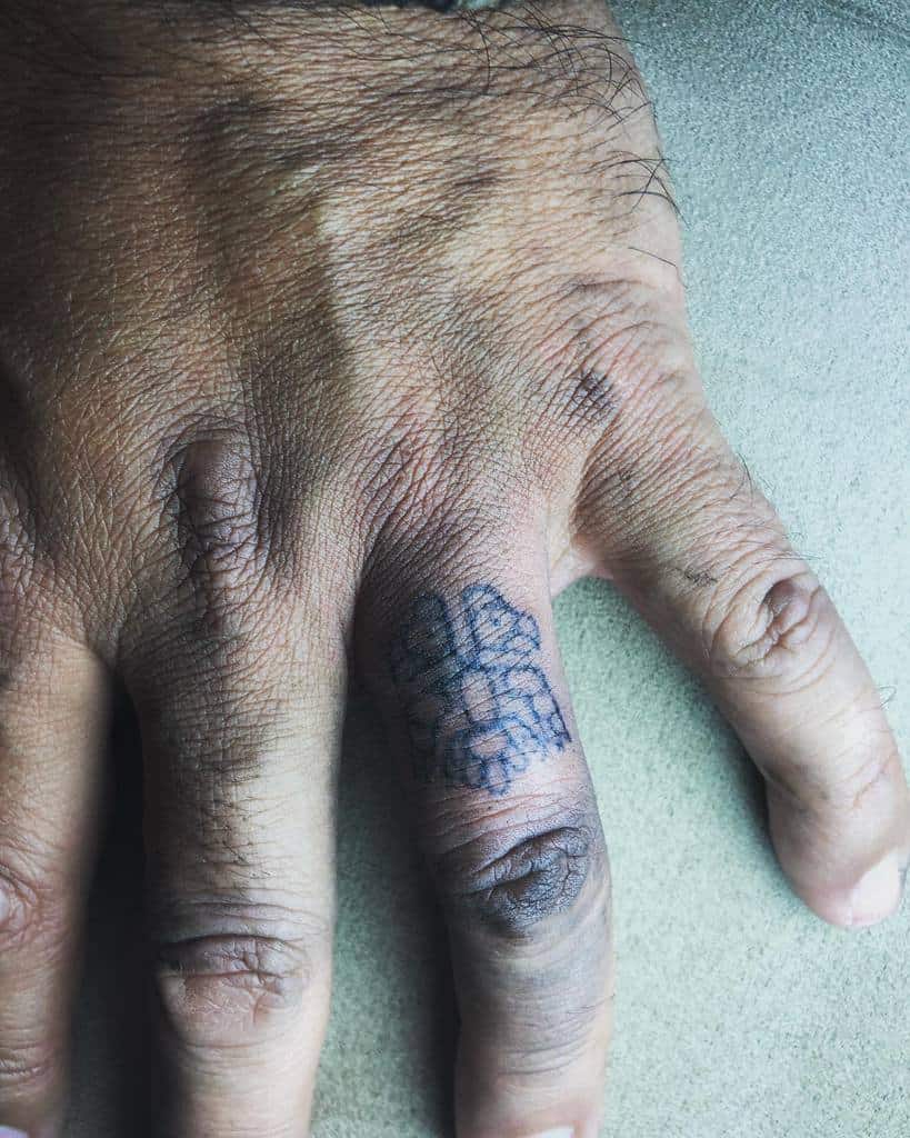 A wedding ring tattoo of a detailed design, possibly a tribal or symbolic pattern, placed on the side of the finger