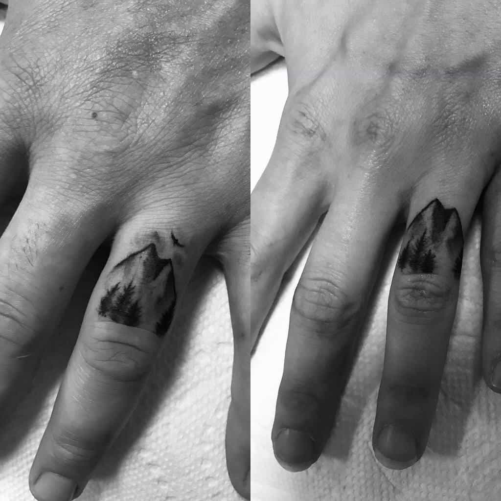 Matching wedding ring tattoos of mountain landscapes with trees and birds, in a black-and-white design
