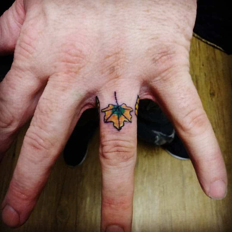 A vibrant wedding ring tattoo of a colorful leaf on the finger, symbolizing nature and the changing seasons