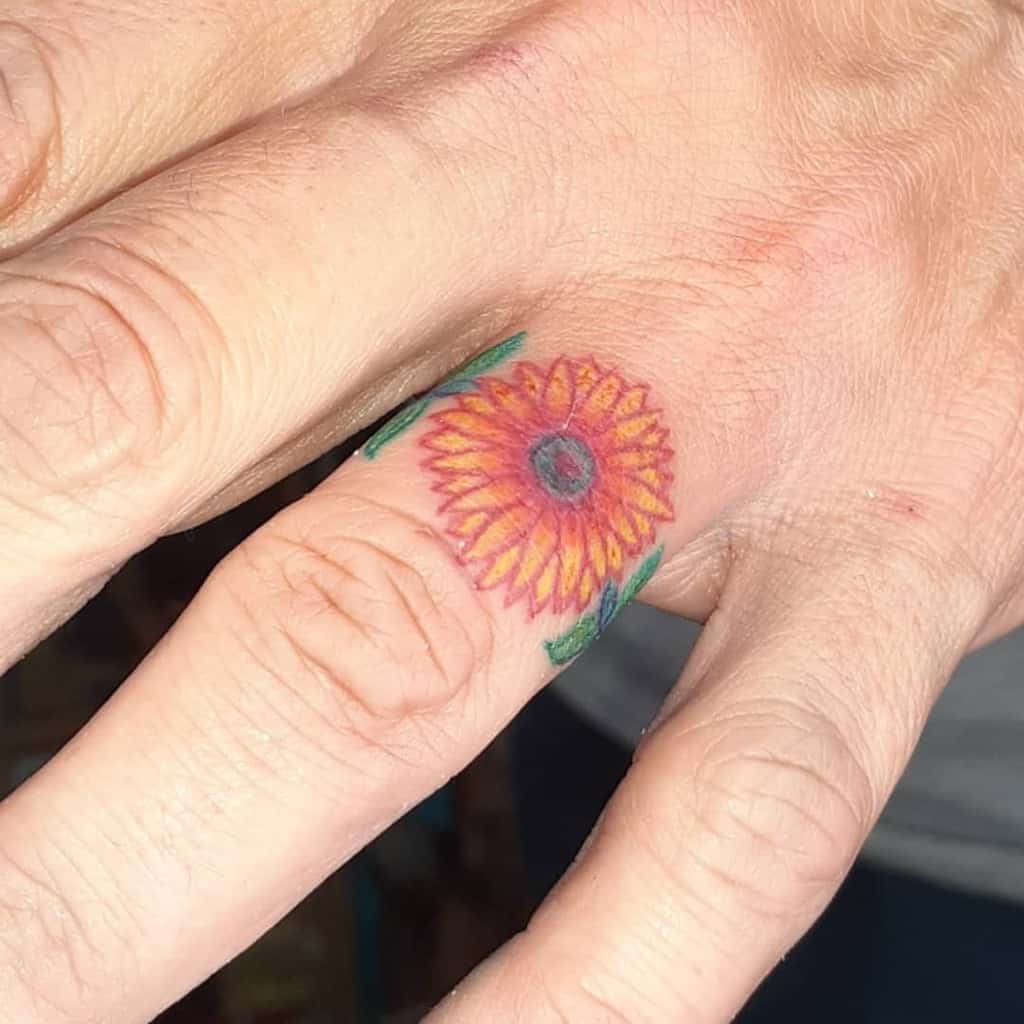 A colorful wedding ring tattoo of a sunflower on the finger, symbolizing happiness, growth, and positivity