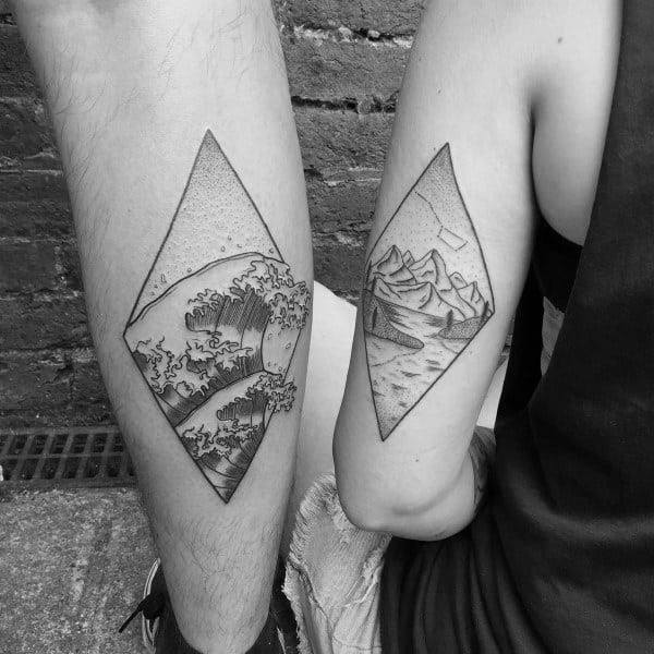 Matching diamond-shaped tattoos of a wave and a mountain landscape, symbolizing the balance of strength and calm in a loving relationship.