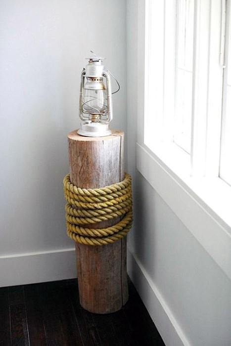 A rustic lantern on a wooden post wrapped with rope, next to a white-framed window in a corner