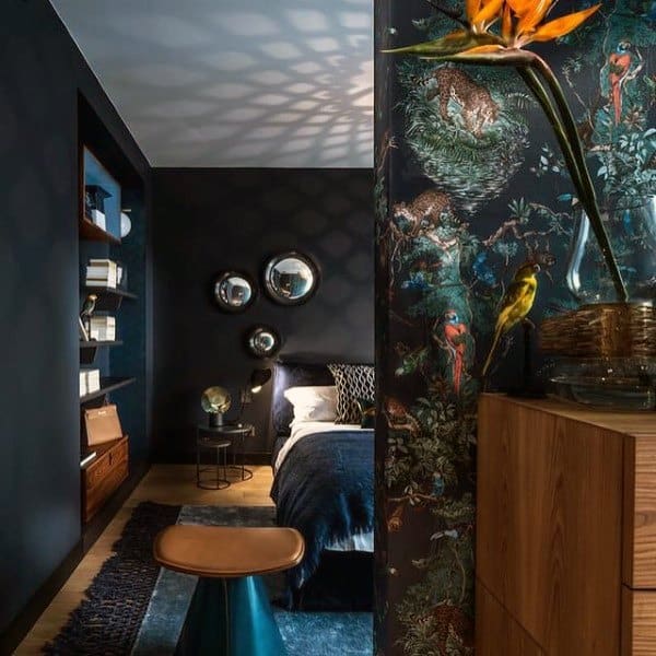 Dark navy bedroom with tropical wallpaper, round mirrors, and stylish wooden furniture.