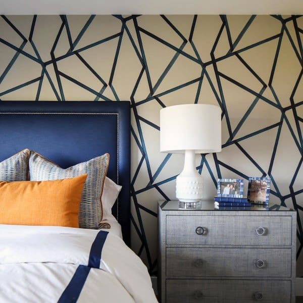 Navy and white bedroom with geometric wallpaper, leather headboard, and modern bedside lamp.