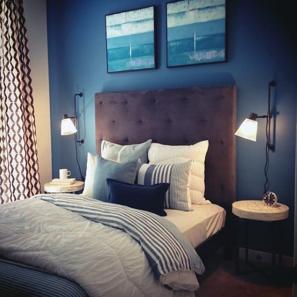 Cozy navy bedroom with striped bedding, tufted headboard, and wall-mounted reading lamps.