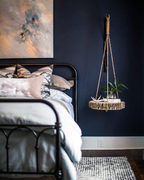 Cozy bedroom with navy walls, metal bed frame, and hanging rope shelf with plant decor.