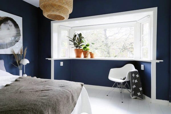 Minimal navy bedroom with a bright bay window, plants, and cozy textures.