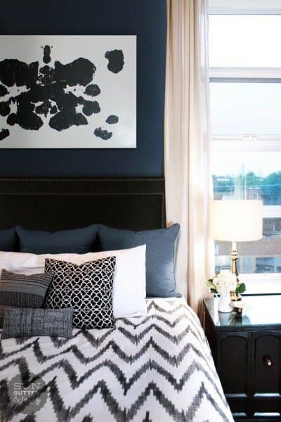 Stylish bedroom with navy accent wall, abstract artwork, and chevron-patterned bedding.