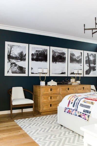 Navy bedroom with wooden dresser, black-and-white landscape art, and patterned area rug.
