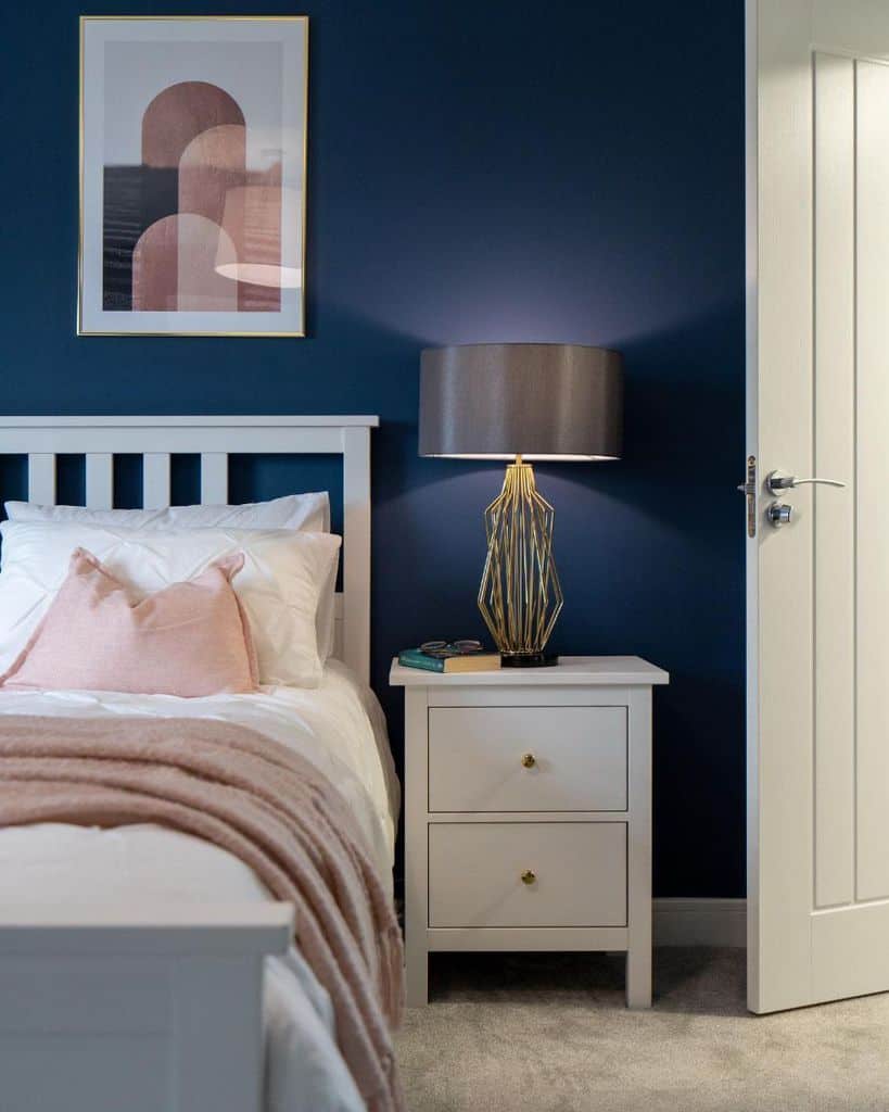 Elegant navy blue bedroom with a soft pink accent and modern gold lamp.