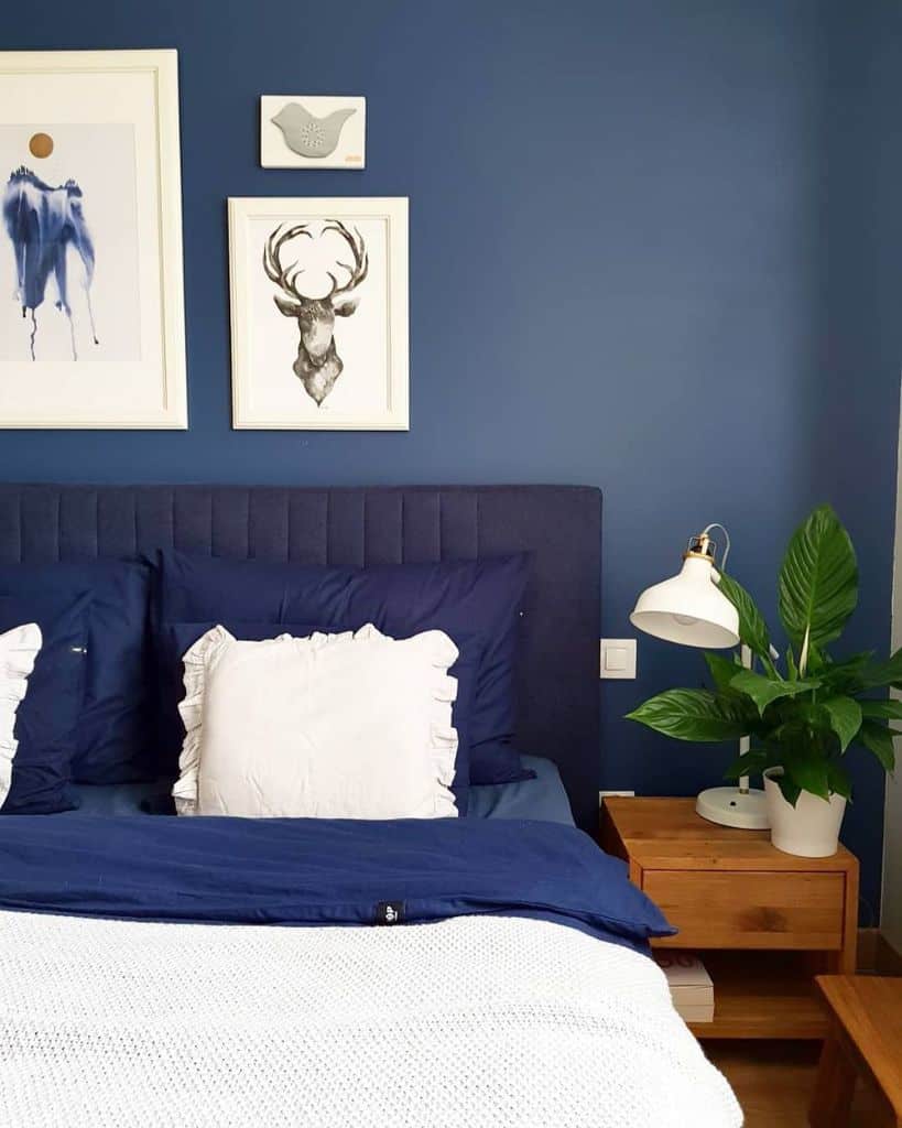 Stylish navy blue bedroom with cozy bedding, framed wall art, and fresh greenery for a calm ambiance.
