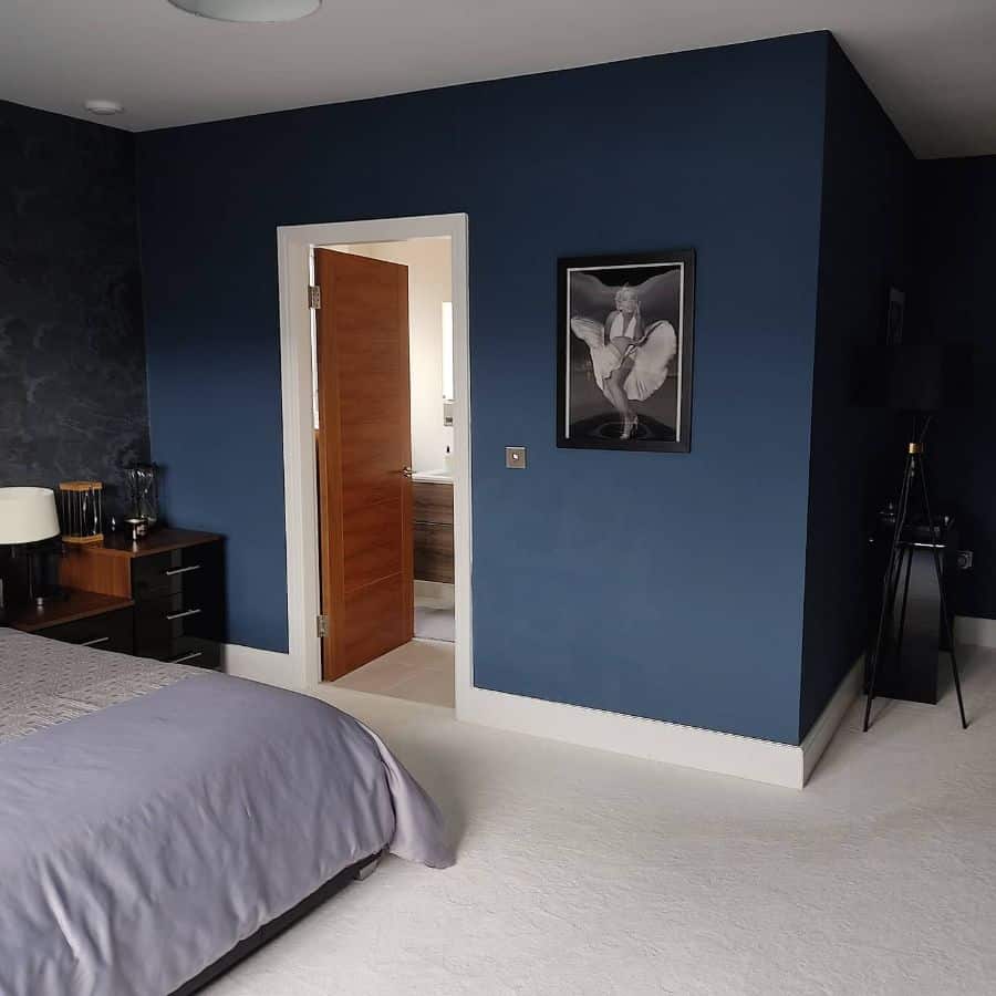 Modern navy blue bedroom featuring clean lines, wooden door, monochrome artwork, and elegant black furniture.