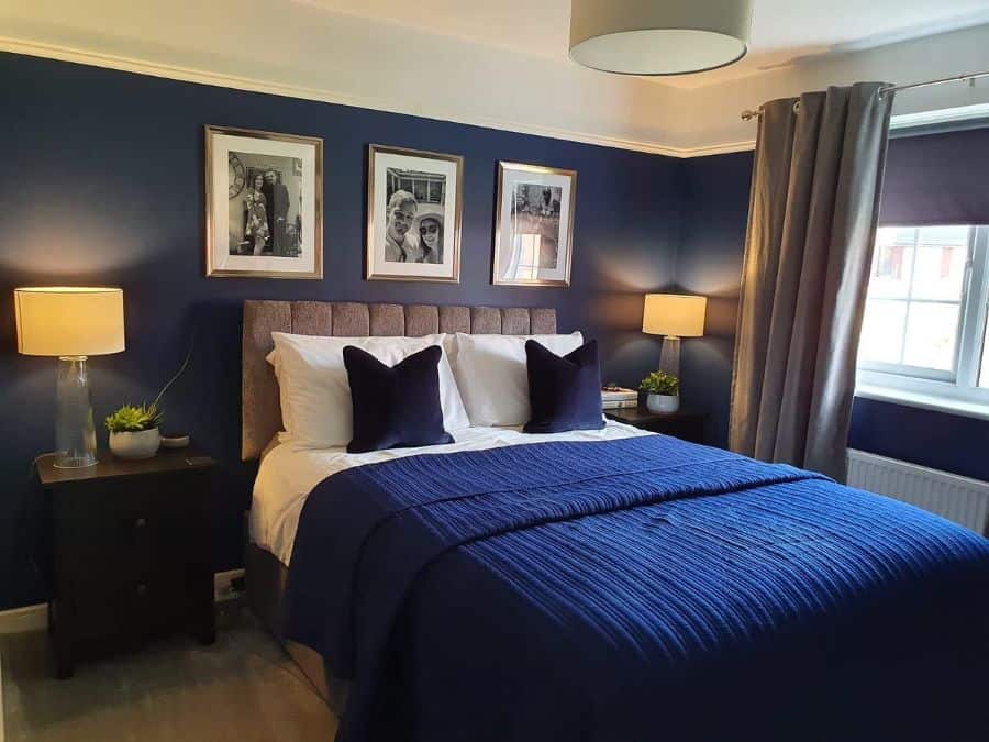 Navy blue bedroom with cozy bedding, framed photos, and soft lighting.