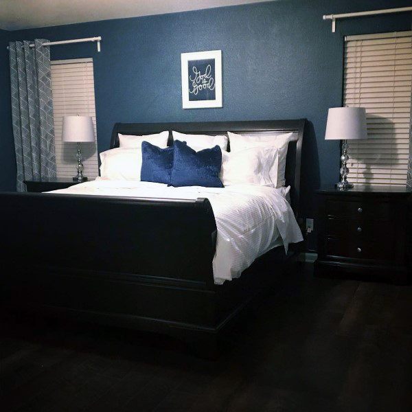 Classic navy bedroom with white bedding, dark wooden furniture, and framed wall art.