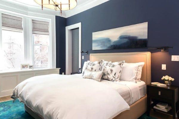 Elegant bedroom with navy blue walls, beige upholstered bed, and large bay windows.