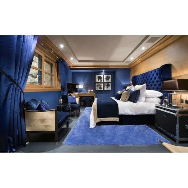 Elegant blue bedroom with tufted headboard, lounge area, and warm wood finishes.