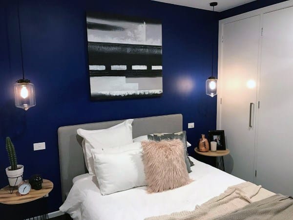 Stylish navy bedroom with soft bedding, pendant lights, and modern wall art.