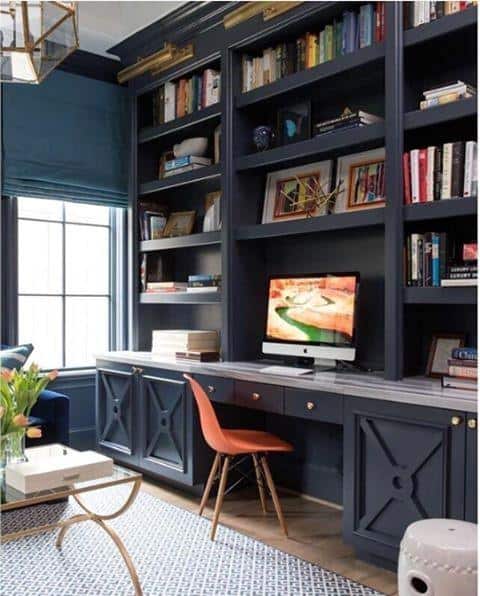 Home office featuring a built-in desk, dark blue bookshelf, orange chair, and window with a blue blind