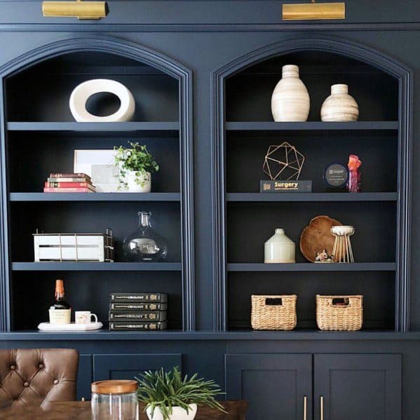 Stylish navy blue built-in bookcases with arch detailing, featuring a mix of decorative vases, books, and baskets for an organized yet chic office look