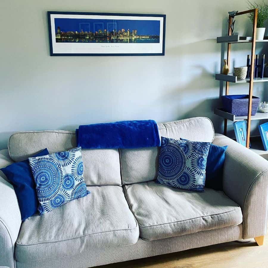 Neutral-toned sofa with blue throw pillows, wall art, and a modern shelf in the background.