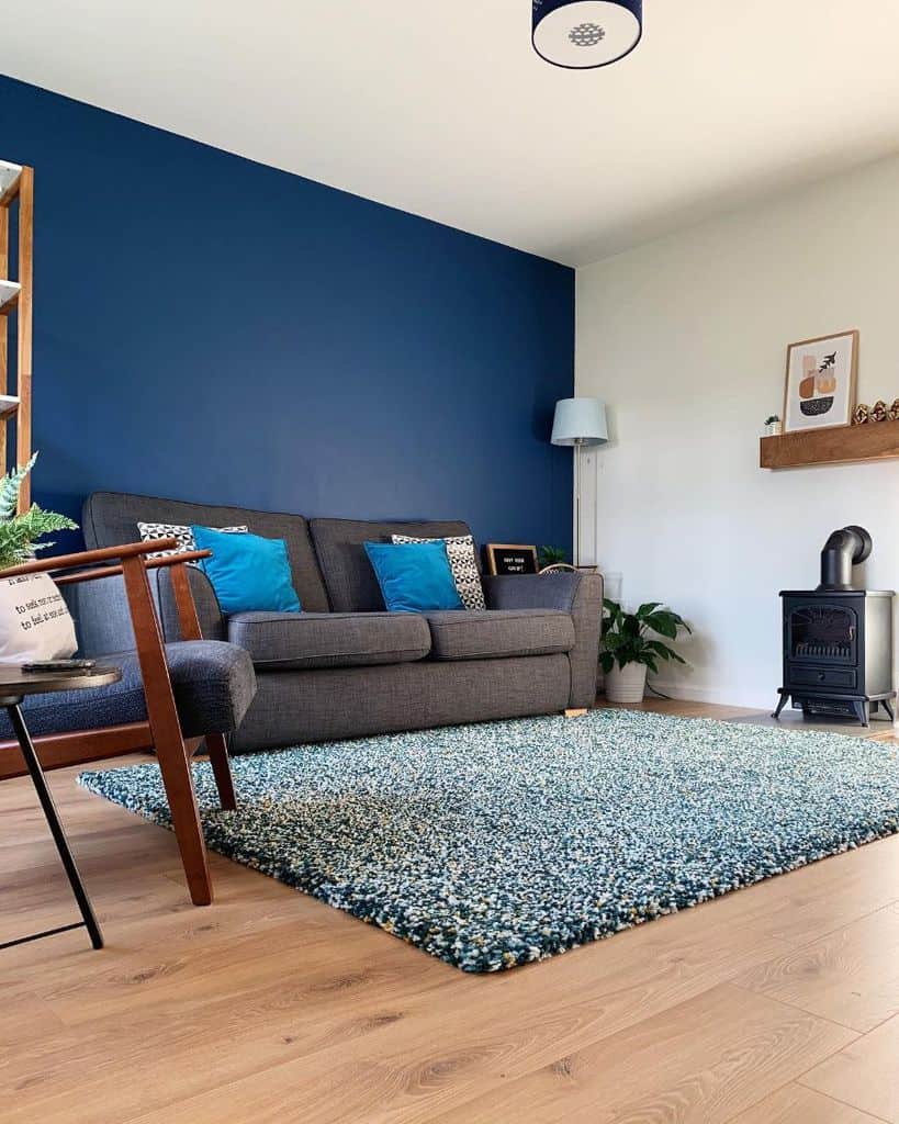 Modern living room with navy accent wall, grey sofa, blue cushions, and textured rug.