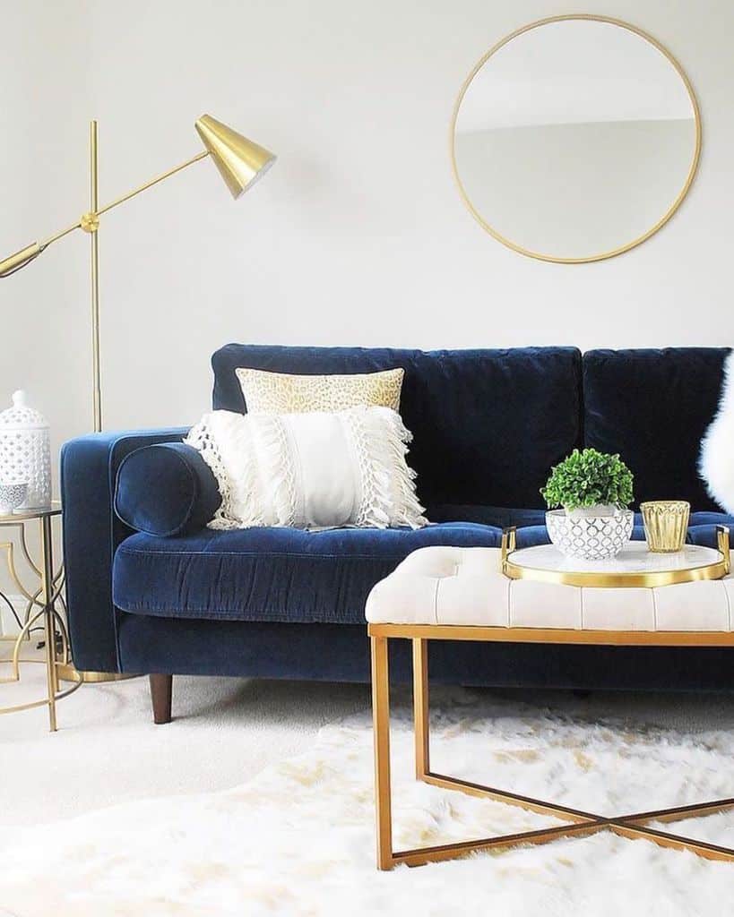 Stylish living room with navy blue sofa, gold accents, and round wall mirror.