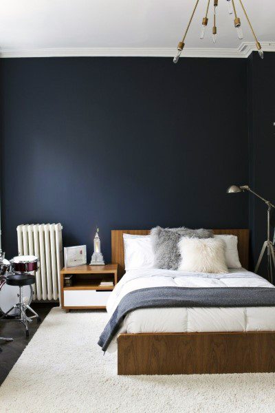Modern navy bedroom with wooden bed frame, fluffy pillows, and sleek floor lamp.