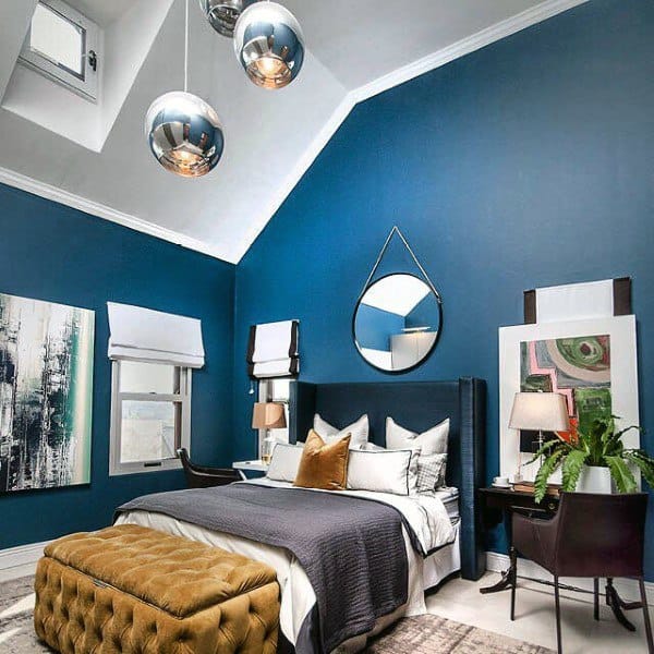 Navy-themed bedroom with vaulted ceilings, metallic accents, and a cozy tufted ottoman.