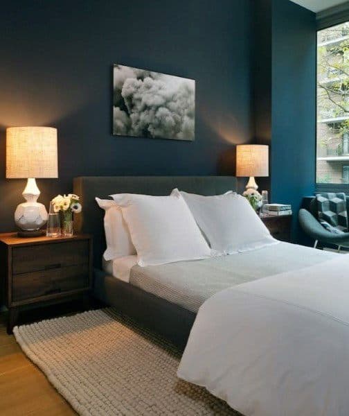 Cozy bedroom with navy walls and warm lighting from bedside lamps, creating a serene and inviting atmosphere.