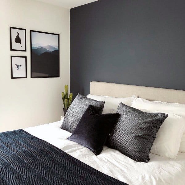 Modern bedroom with navy accent wall, framed art, and layered black and gray pillows on white bedding.