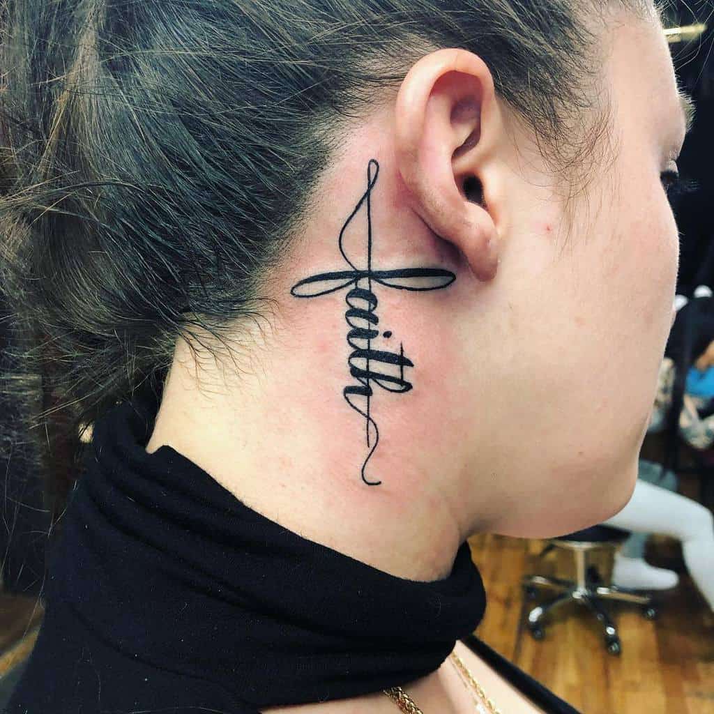 A tattoo of the word "faith" in elegant cursive script behind a woman's ear