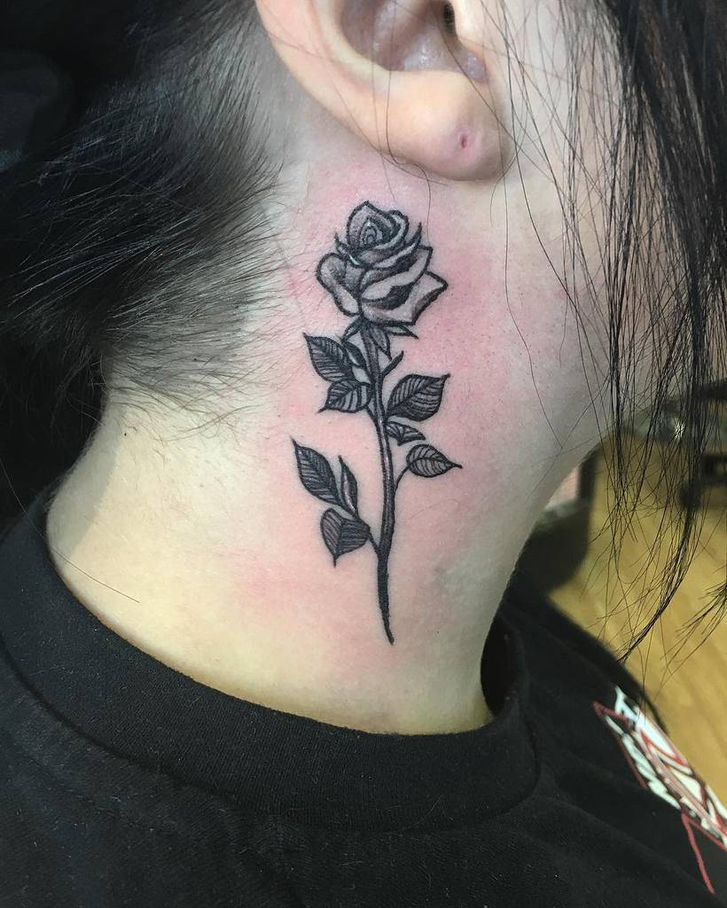 Neck tattoo of a detailed black rose with leaves elegantly extending from the stem