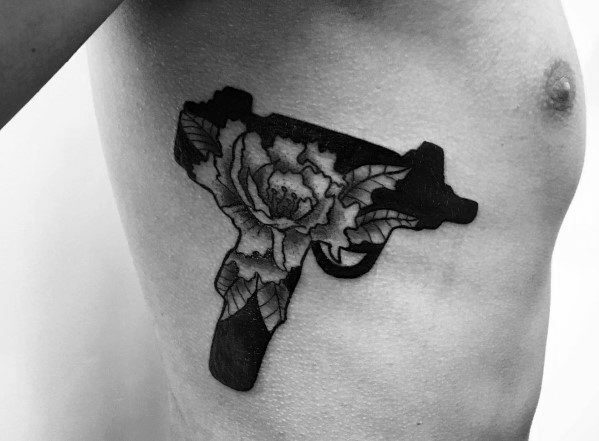 Black Uzi tattoo on the ribcage with a detailed floral design inside, blending bold firearm imagery with delicate botanical elements.