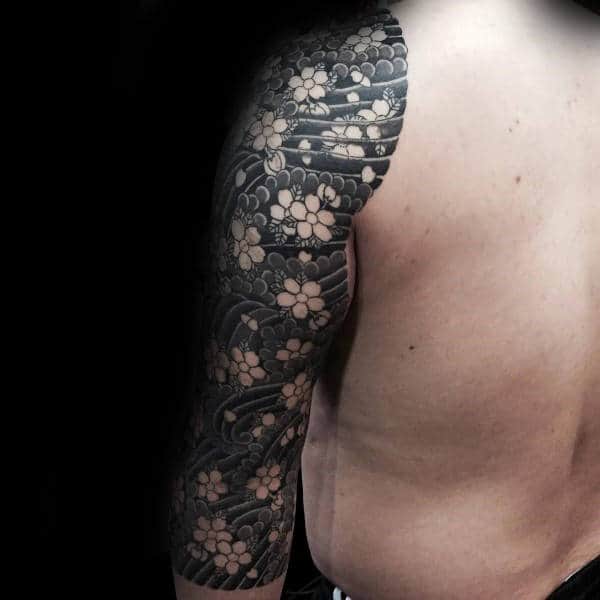 Japanese-style half-sleeve tattoo using negative space to create intricate cherry blossoms against bold black shading and flowing wave patterns