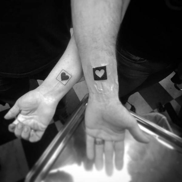 Matching wrist tattoos of hearts inside card suit frames, symbolizing love, luck, and a strong bond like a perfect pair in a deck.