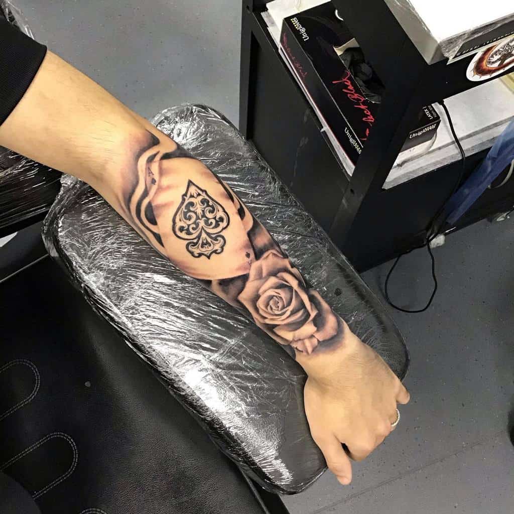 A black-and-white tattoo of the Ace of Spades card surrounded by roses, with intricate shading