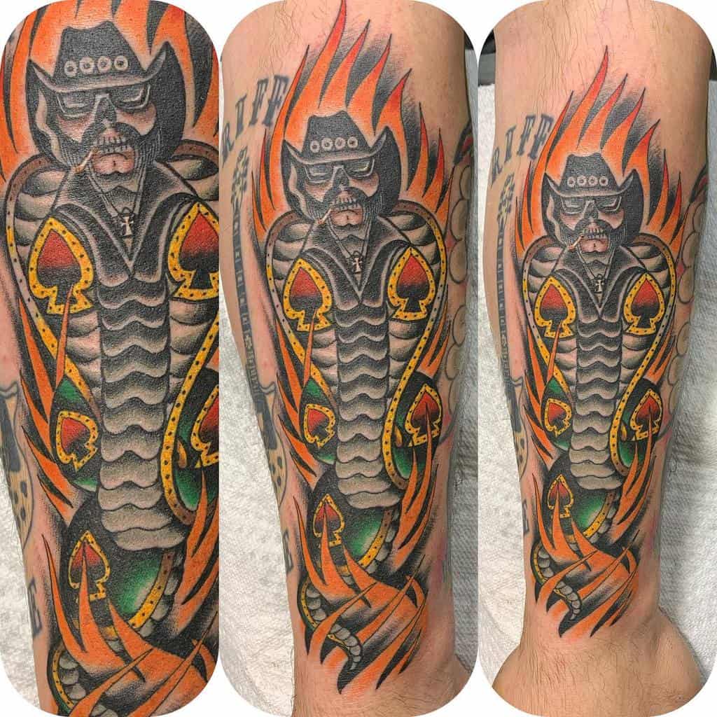 A colorful tattoo of a man snake wearing a cowboy hat and surrounded by flames, with Ace of Spades symbols