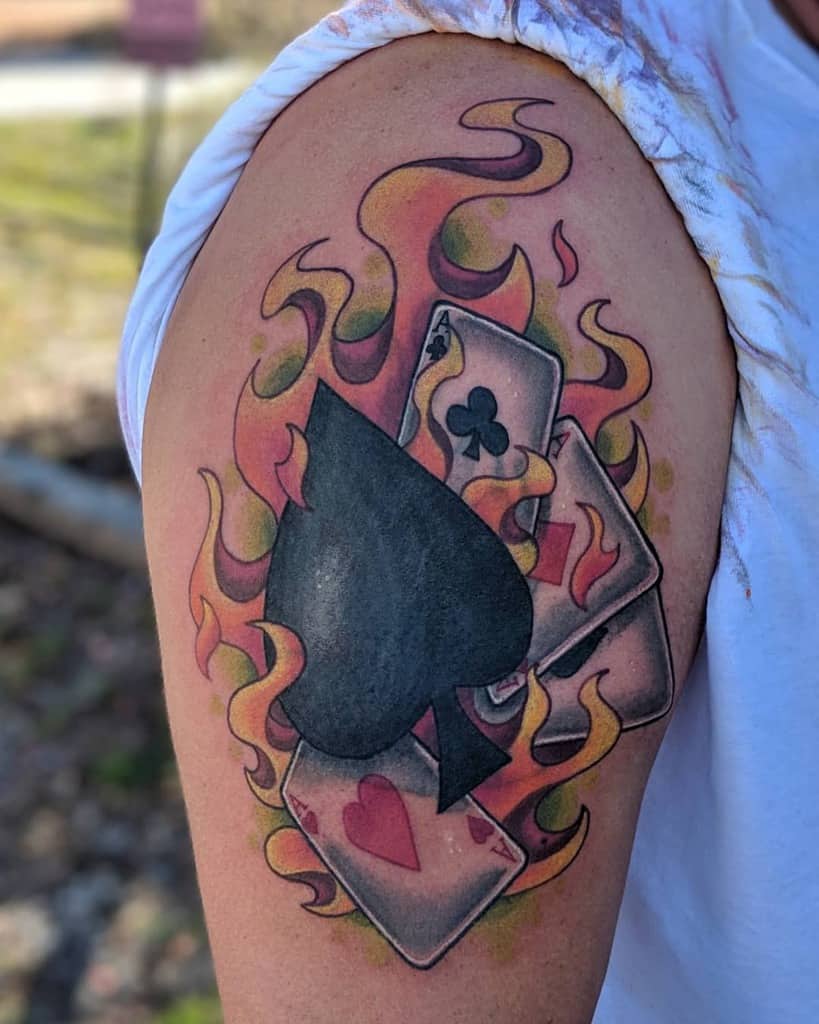 A colorful tattoo of the Ace of Spades card surrounded by flames, with additional cards featuring hearts, diamond and clubs