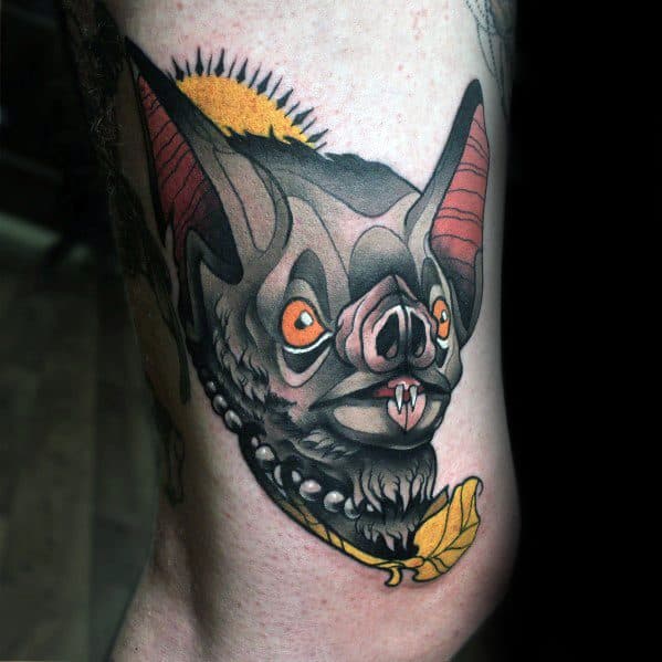 Neo-traditional bat tattoo with wide orange eyes, large red ears, a pearl necklace, yellow leaf, and a rising sun in the background.