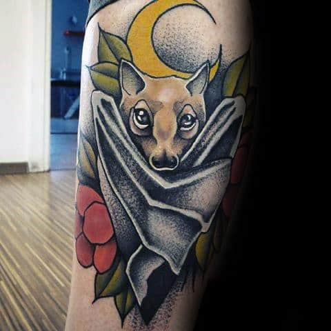Neo-traditional tattoo of a bat wrapped in wings with bold eyes, surrounded by leaves, red flowers, and a yellow crescent moon.