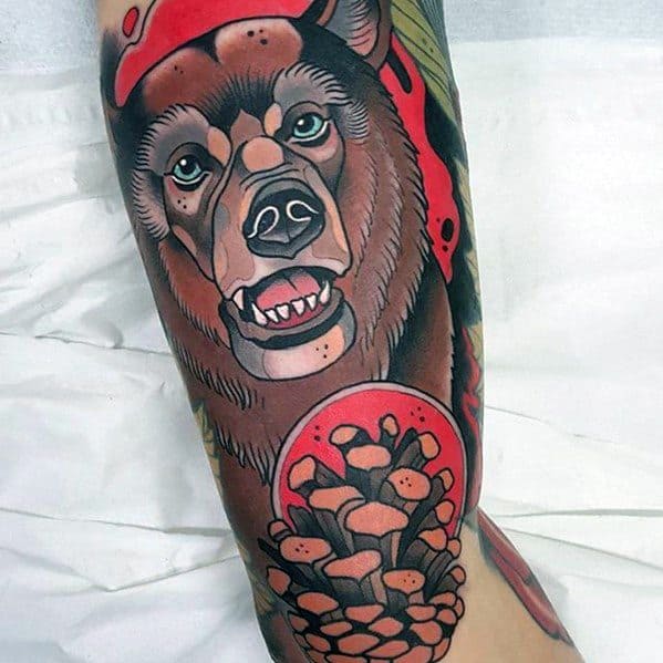 Neo-traditional bear tattoo featuring a detailed bear with piercing green eyes, a red background, and a bold pinecone design on the forearm.