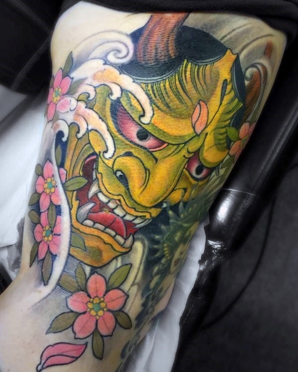 Neo-traditional arm tattoo featuring a fierce yellow Hannya mask, vibrant pink cherry blossoms, swirling waves, and bold Japanese-style shading