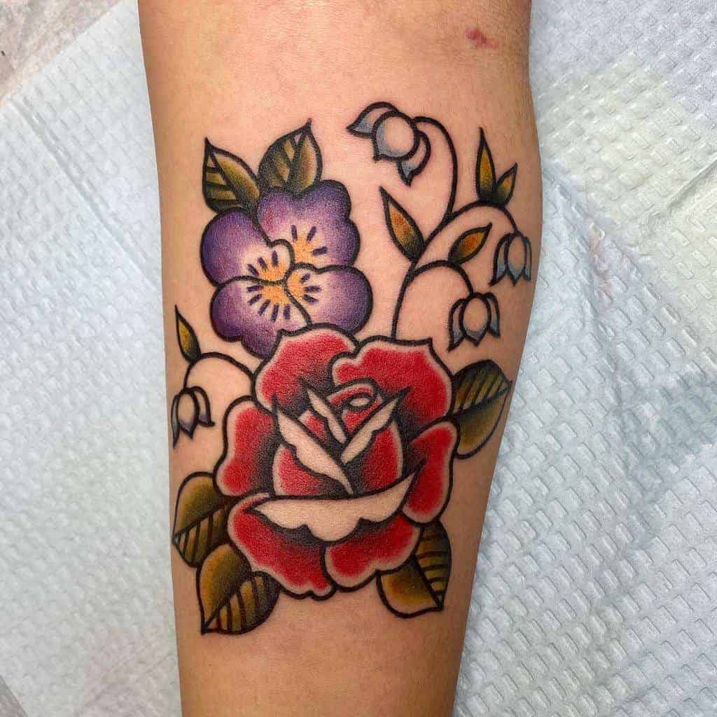 Neo-traditional tattoo featuring vibrant red and purple flowers with green leaves, accented by delicate lilies of the valley